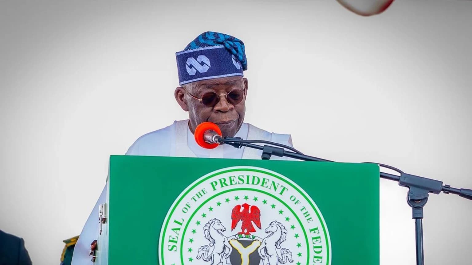Nigerian President Bola Tinubu speaking at a podium bearing the presidential seal