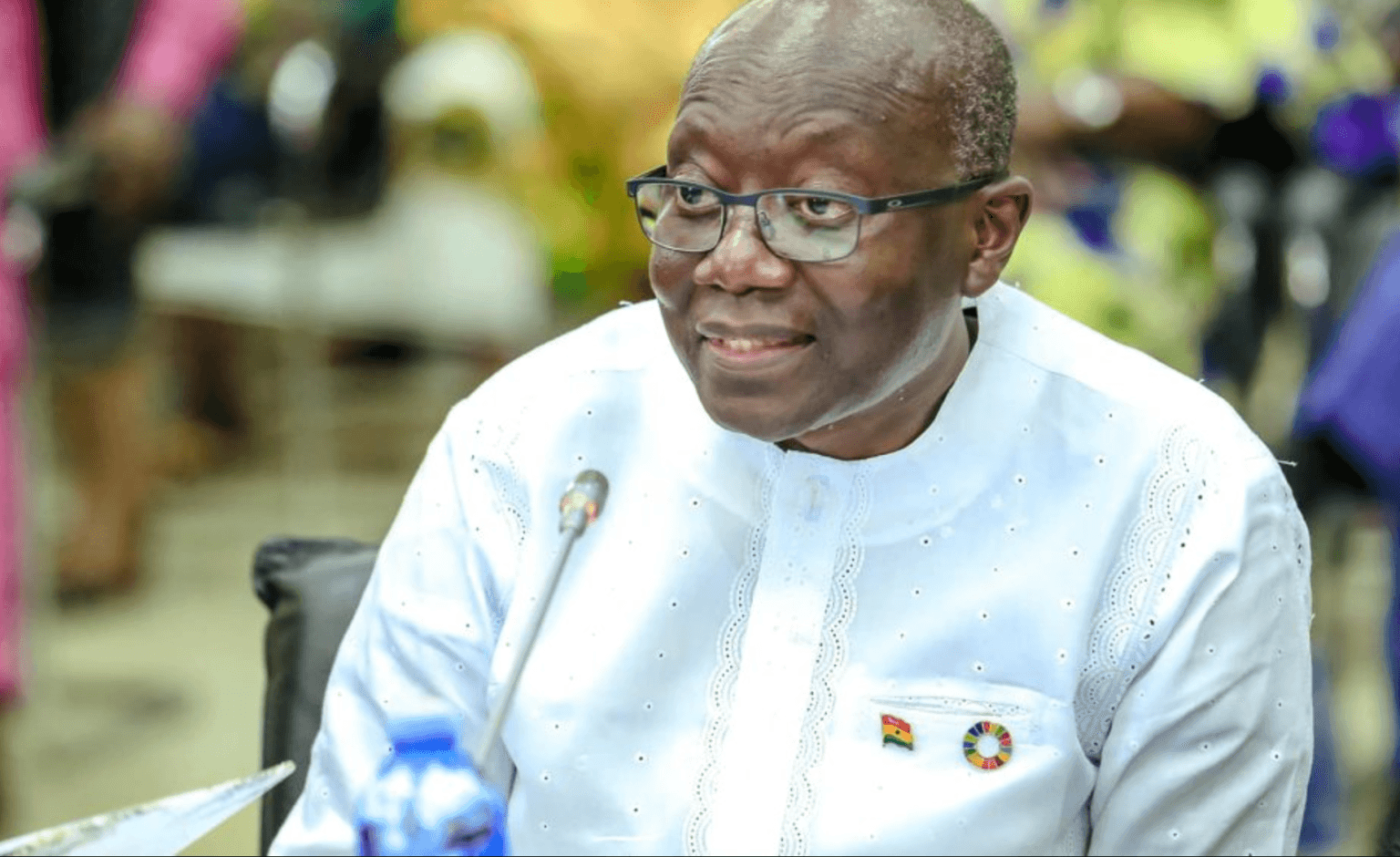 Ghana's former Finance Minister Ken Ofori-Atta smiling while seated at a podium with a microphone