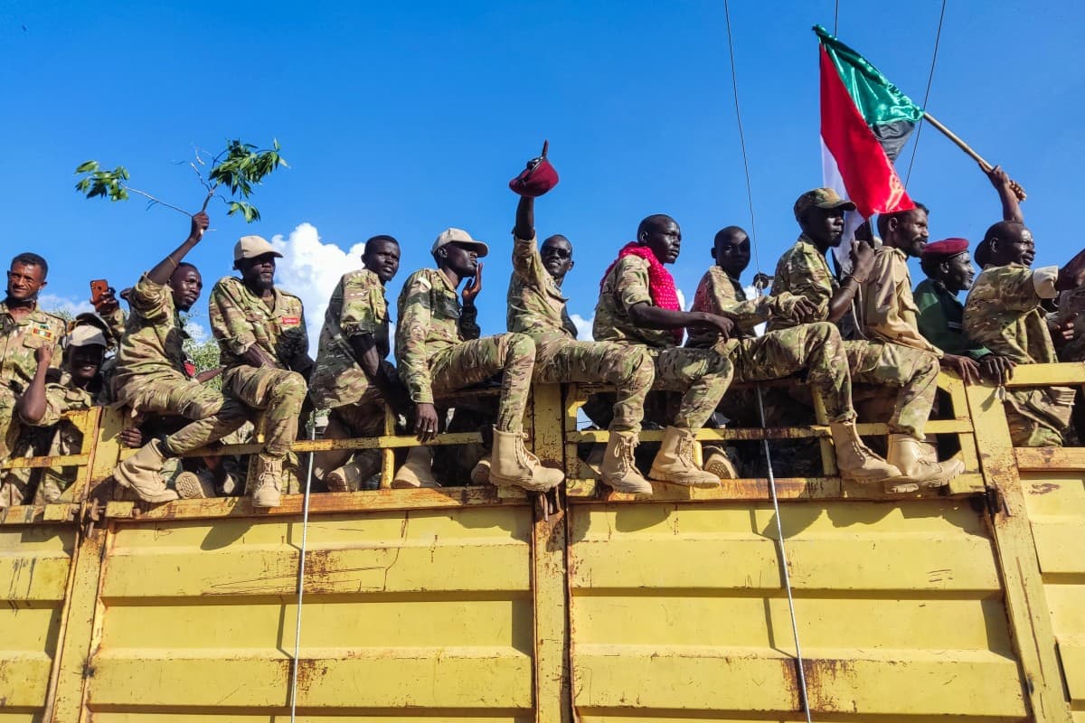 Armed fighters riding atop a truck, one waving a Sudanese flag